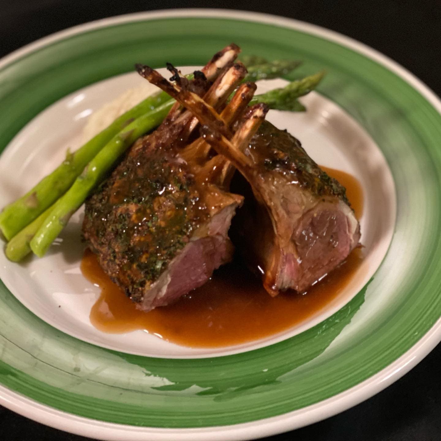 Pan-roasted lamb pops plated with asparagus and whipped yukons, on a green-rimmed plate at The Mansard