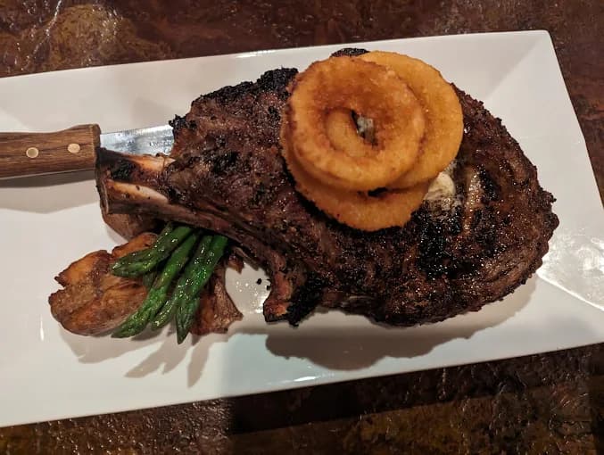A char-grilled bone-in ribeye plated with onion rings and asparagus at The Mansard